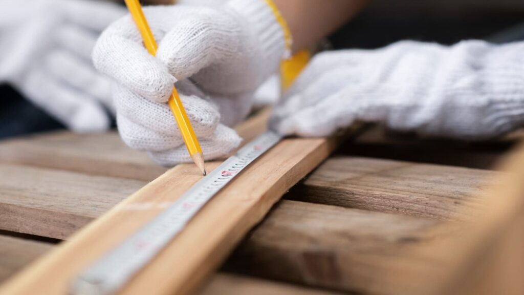 Handen met werkhandschoenen meten hout af voor het maken van een klaptafel