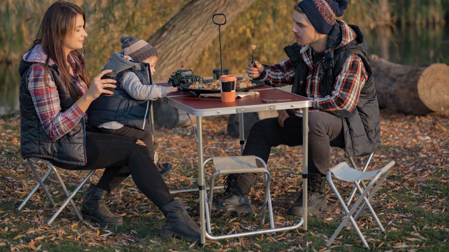 Gezin zit aan een klaptafel in de natuur tijdens een picknickmoment in de herfst