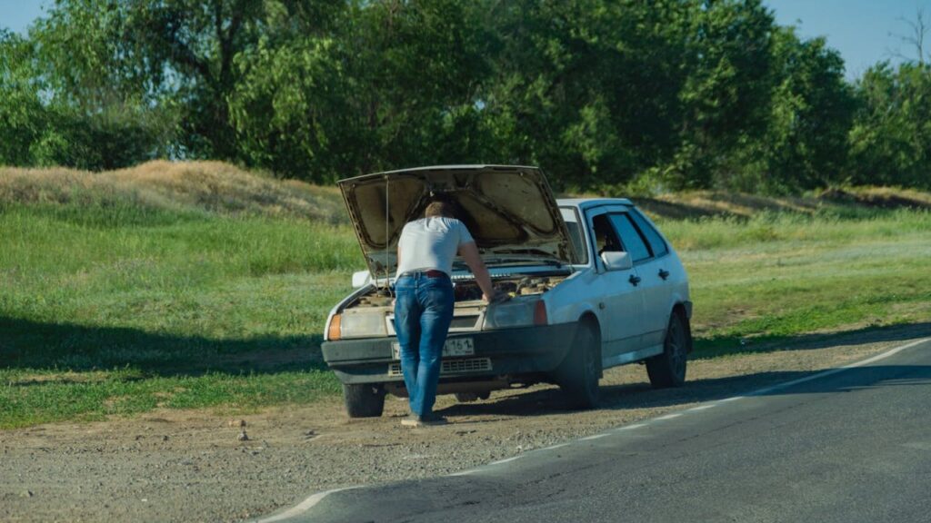 Autopech veilig handelen bij stilgevallen auto langs de weg terwijl bestuurder onder motorkap kijkt