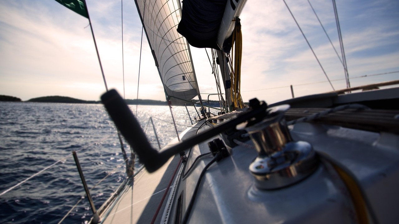 Zeilboot vaart schuin op open water met volle zeilen bij ondergaande zon, symbool voor stuurvertrouwen