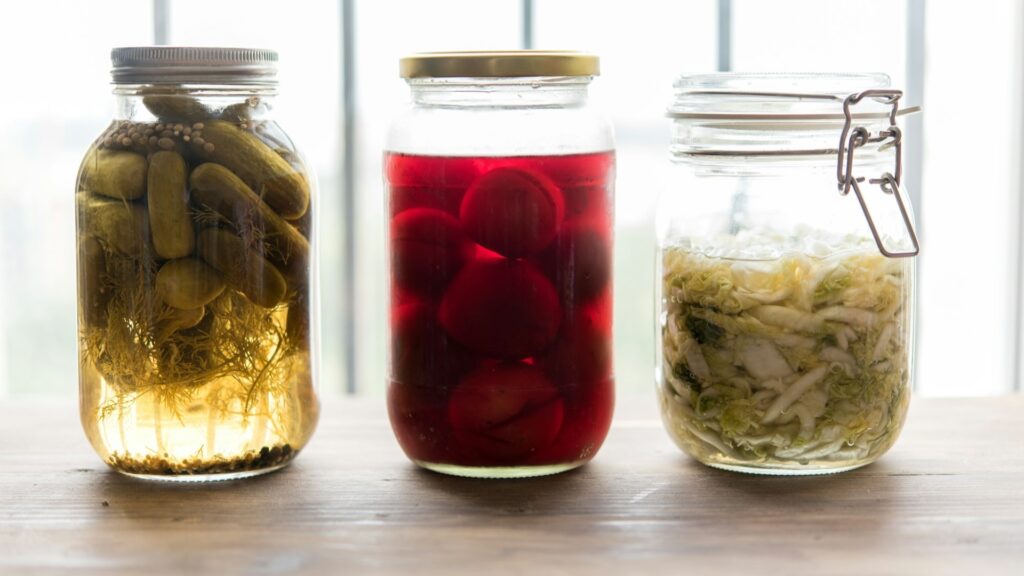 Drie glazen potten met gefermenteerde komkommer, rode biet en kool tijdens fermenteren op tafel