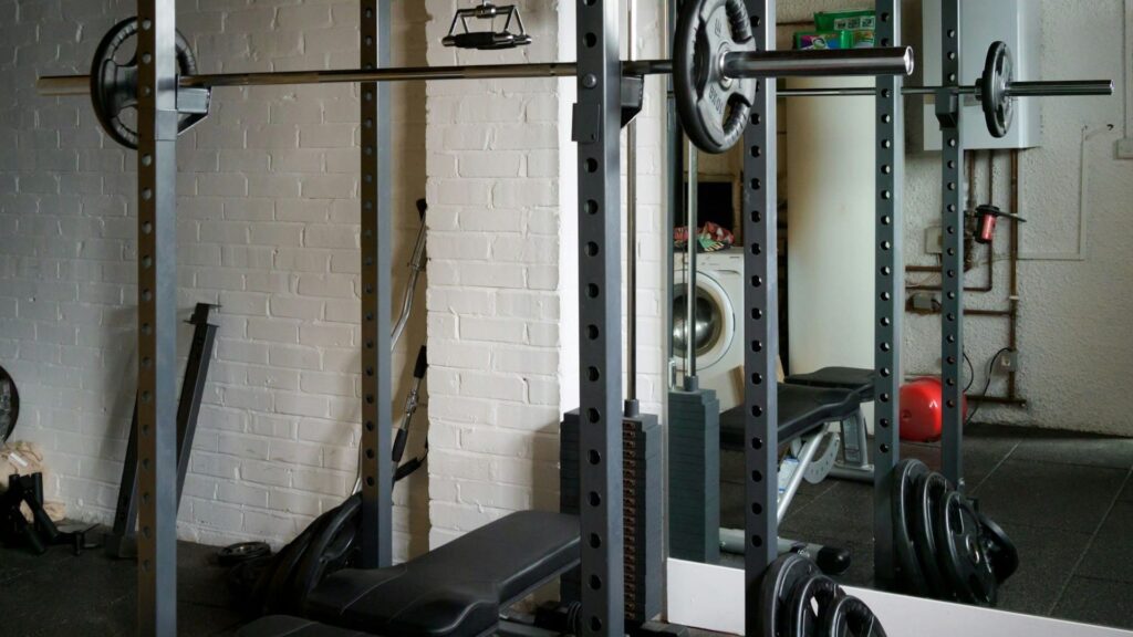 Thuisgym met halterbank, squat rack en gewichten tegen witte muur