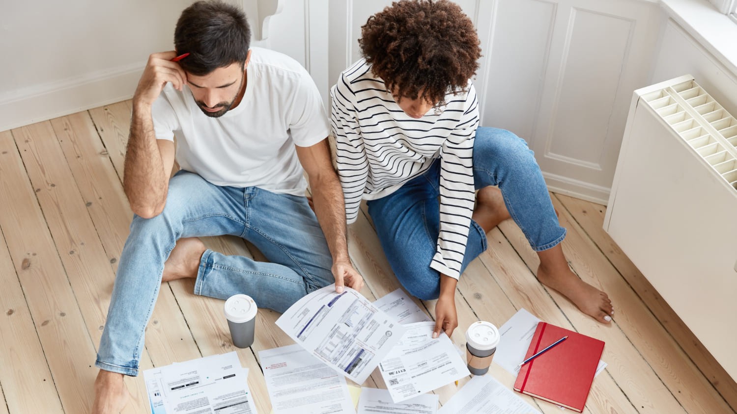 Koppel zit op de vloer tussen rekeningen, mogelijk bezig met plannen voor woning leeghalen