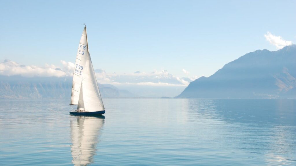 Zeilboot op kalm water met bergen op de achtergrond, rust en stuurvertrouwen in balans